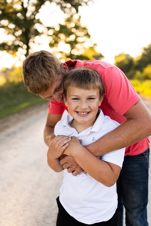 Family walking together through a field in High Hill Missouri
Parents smiling at their child while standing on a gravel road
Child laughing and making a silly face during a family session
Family holding hands in tall grass with warm evening light
Parents hugging their child while standing on a quiet country road