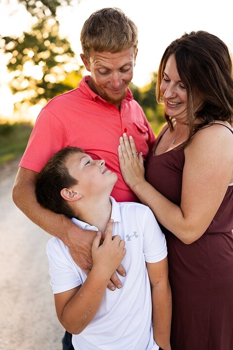 Family walking together through a field in High Hill Missouri
Parents smiling at their child while standing on a gravel road
Child laughing and making a silly face during a family session
Family holding hands in tall grass with warm evening light
Parents hugging their child while standing on a quiet country road