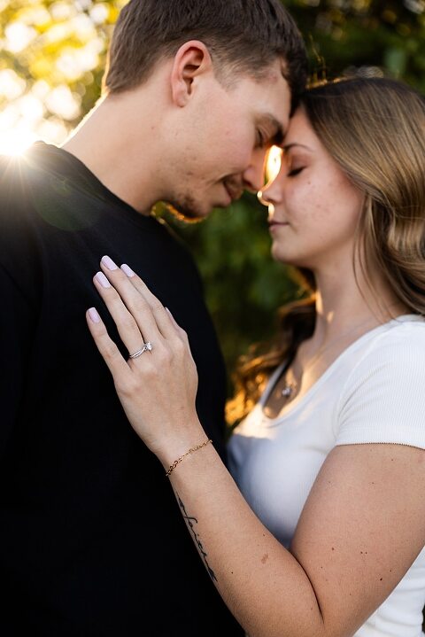 Tyler and Grace standing on a sunlit path at Towne Park during their engagement session.
Couple laughing together in an open field at Towne Park.
Tyler and Grace holding hands along a wooded trail with soft golden light behind them.
Close–up of the couple smiling at each other during their engagement session.
Engagement ring photo taken at Towne Park with natural greenery in the background.