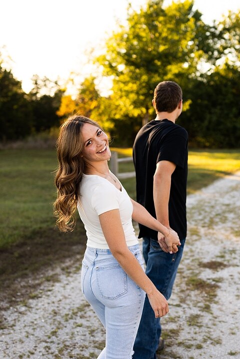 Tyler and Grace standing on a sunlit path at Towne Park during their engagement session.
Couple laughing together in an open field at Towne Park.
Tyler and Grace holding hands along a wooded trail with soft golden light behind them.
Close–up of the couple smiling at each other during their engagement session.
Engagement ring photo taken at Towne Park with natural greenery in the background.