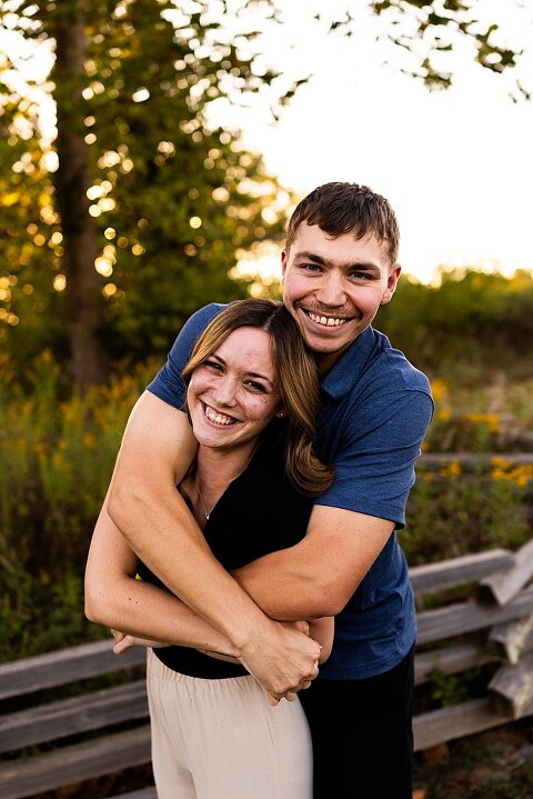 Tyler and Grace standing on a sunlit path at Towne Park during their engagement session.
Couple laughing together in an open field at Towne Park.
Tyler and Grace holding hands along a wooded trail with soft golden light behind them.
Close–up of the couple smiling at each other during their engagement session.
Engagement ring photo taken at Towne Park with natural greenery in the background.