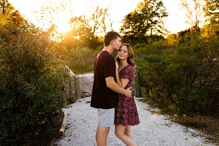 Tyler and Grace standing on a sunlit path at Towne Park during their engagement session.
Couple laughing together in an open field at Towne Park.
Tyler and Grace holding hands along a wooded trail with soft golden light behind them.
Close–up of the couple smiling at each other during their engagement session.
Engagement ring photo taken at Towne Park with natural greenery in the background.