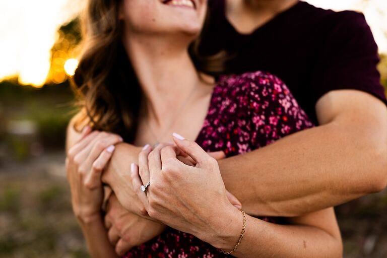 Tyler and Grace standing on a sunlit path at Towne Park during their engagement session.
Couple laughing together in an open field at Towne Park.
Tyler and Grace holding hands along a wooded trail with soft golden light behind them.
Close–up of the couple smiling at each other during their engagement session.
Engagement ring photo taken at Towne Park with natural greenery in the background.