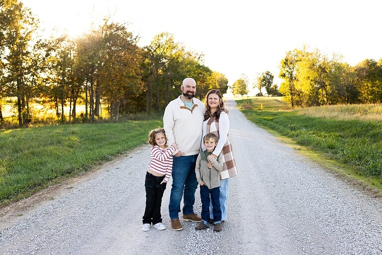 Family standing together on a gravel road in High Hill Missouri.
Kids smiling and walking down a sunny gravel path.
Mom hugging her two kids during their gravel road session.
Children running through a field beside a country road.
Family laughing together in warm evening light.