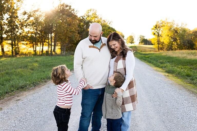 Family standing together on a gravel road in High Hill Missouri.
Kids smiling and walking down a sunny gravel path.
Mom hugging her two kids during their gravel road session.
Children running through a field beside a country road.
Family laughing together in warm evening light.