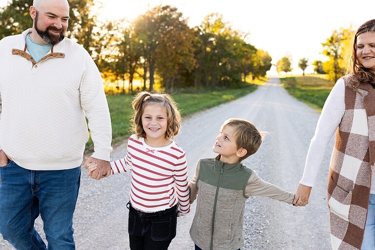 Family standing together on a gravel road in High Hill Missouri.
Kids smiling and walking down a sunny gravel path.
Mom hugging her two kids during their gravel road session.
Children running through a field beside a country road.
Family laughing together in warm evening light.