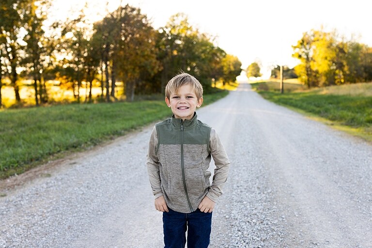 Family standing together on a gravel road in High Hill Missouri.
Kids smiling and walking down a sunny gravel path.
Mom hugging her two kids during their gravel road session.
Children running through a field beside a country road.
Family laughing together in warm evening light.