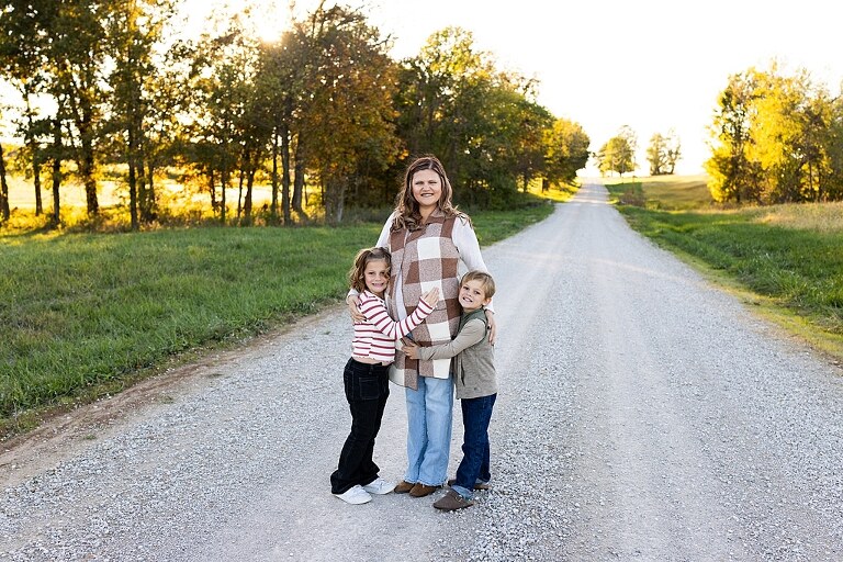 Family standing together on a gravel road in High Hill Missouri.
Kids smiling and walking down a sunny gravel path.
Mom hugging her two kids during their gravel road session.
Children running through a field beside a country road.
Family laughing together in warm evening light.