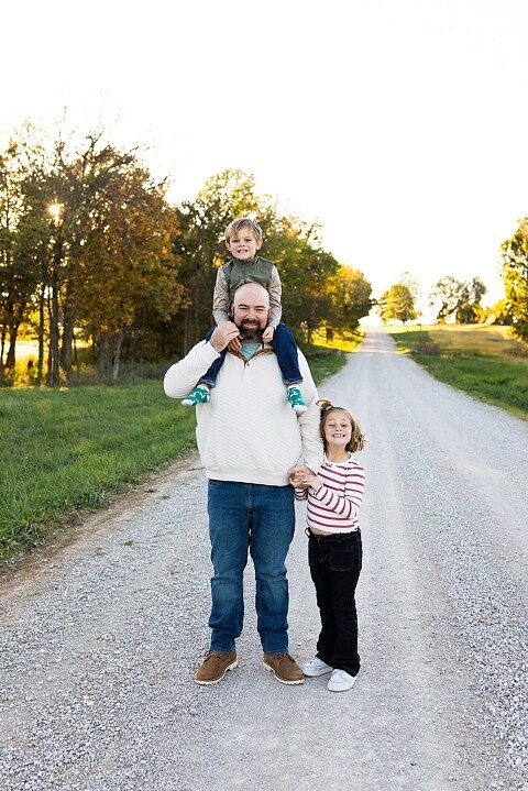 Family standing together on a gravel road in High Hill Missouri.
Kids smiling and walking down a sunny gravel path.
Mom hugging her two kids during their gravel road session.
Children running through a field beside a country road.
Family laughing together in warm evening light.