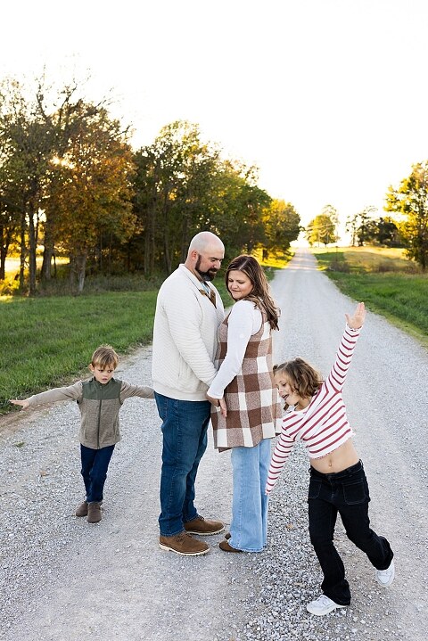 Family standing together on a gravel road in High Hill Missouri.
Kids smiling and walking down a sunny gravel path.
Mom hugging her two kids during their gravel road session.
Children running through a field beside a country road.
Family laughing together in warm evening light.