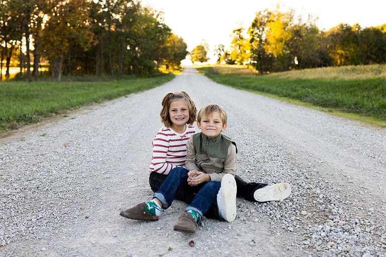 Family standing together on a gravel road in High Hill Missouri.
Kids smiling and walking down a sunny gravel path.
Mom hugging her two kids during their gravel road session.
Children running through a field beside a country road.
Family laughing together in warm evening light.