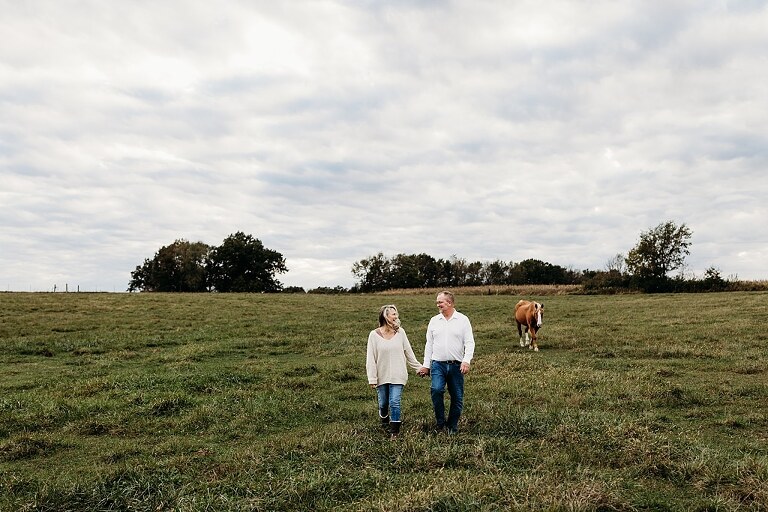 Couple standing together on their new country property during golden hour.
Tina and Jimmy laughing together beside a tall tree line.
Couple posing with one of their farm animals in soft evening light.
Tina and Jimmy walking hand in hand across their open field.
Close-up of the couple smiling with their animals nearby.