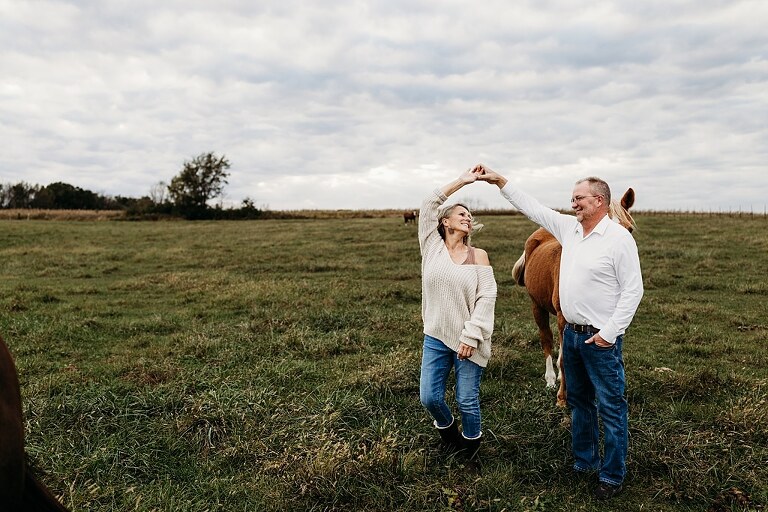 Couple standing together on their new country property during golden hour.
Tina and Jimmy laughing together beside a tall tree line.
Couple posing with one of their farm animals in soft evening light.
Tina and Jimmy walking hand in hand across their open field.
Close-up of the couple smiling with their animals nearby.