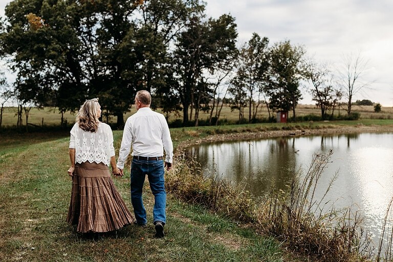 Couple standing together on their new country property during golden hour.
Tina and Jimmy laughing together beside a tall tree line.
Couple posing with one of their farm animals in soft evening light.
Tina and Jimmy walking hand in hand across their open field.
Close-up of the couple smiling with their animals nearby.