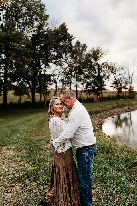 Couple standing together on their new country property during golden hour.
Tina and Jimmy laughing together beside a tall tree line.
Couple posing with one of their farm animals in soft evening light.
Tina and Jimmy walking hand in hand across their open field.
Close-up of the couple smiling with their animals nearby.