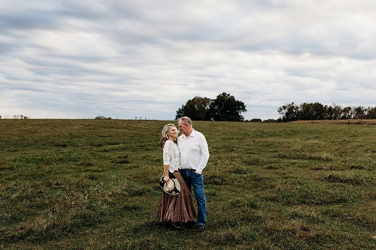 Couple standing together on their new country property during golden hour.
Tina and Jimmy laughing together beside a tall tree line.
Couple posing with one of their farm animals in soft evening light.
Tina and Jimmy walking hand in hand across their open field.
Close-up of the couple smiling with their animals nearby.