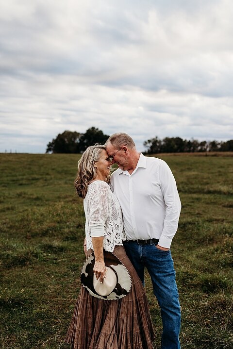 Couple standing together on their new country property during golden hour.
Tina and Jimmy laughing together beside a tall tree line.
Couple posing with one of their farm animals in soft evening light.
Tina and Jimmy walking hand in hand across their open field.
Close-up of the couple smiling with their animals nearby.
