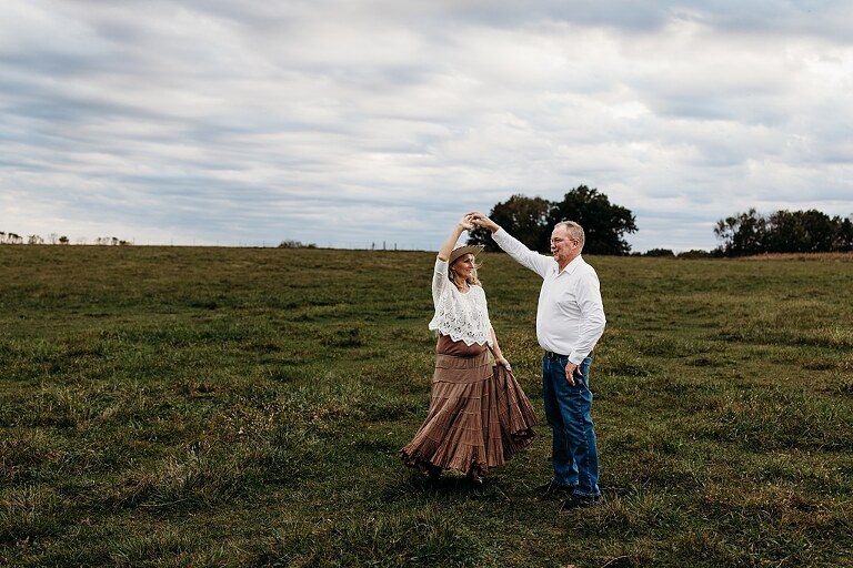 Couple standing together on their new country property during golden hour.
Tina and Jimmy laughing together beside a tall tree line.
Couple posing with one of their farm animals in soft evening light.
Tina and Jimmy walking hand in hand across their open field.
Close-up of the couple smiling with their animals nearby.