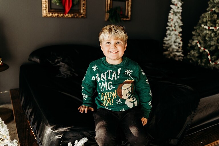 Moody Christmas mini session setup with a black bed and snow-dusted trees.
Five-year-old boy smiling on the Christmas mini session bed.
Close-up of cranberry and popcorn garland on the studio set.
Child surrounded by gold and red Christmas accents in the studio.
Full view of the 2025 Christmas Minis setup in Lake St. Louis Missouri.