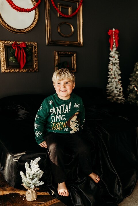 Moody Christmas mini session setup with a black bed and snow-dusted trees.
Five-year-old boy smiling on the Christmas mini session bed.
Close-up of cranberry and popcorn garland on the studio set.
Child surrounded by gold and red Christmas accents in the studio.
Full view of the 2025 Christmas Minis setup in Lake St. Louis Missouri.
