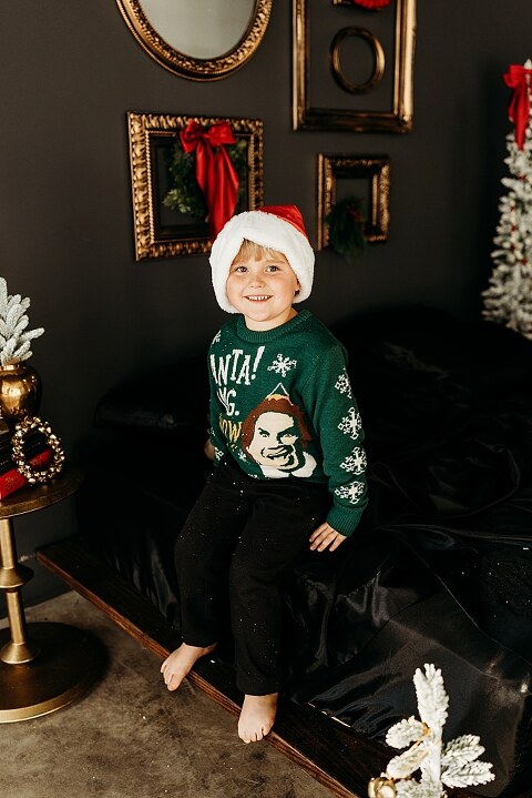 Moody Christmas mini session setup with a black bed and snow-dusted trees.
Five-year-old boy smiling on the Christmas mini session bed.
Close-up of cranberry and popcorn garland on the studio set.
Child surrounded by gold and red Christmas accents in the studio.
Full view of the 2025 Christmas Minis setup in Lake St. Louis Missouri.