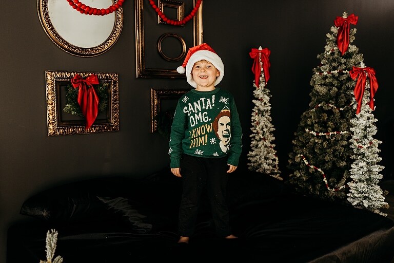 Moody Christmas mini session setup with a black bed and snow-dusted trees.
Five-year-old boy smiling on the Christmas mini session bed.
Close-up of cranberry and popcorn garland on the studio set.
Child surrounded by gold and red Christmas accents in the studio.
Full view of the 2025 Christmas Minis setup in Lake St. Louis Missouri.