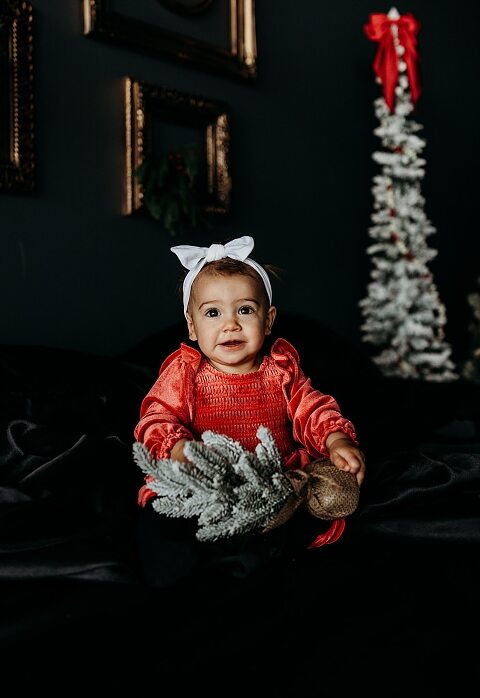 Oden family posing in a moody Christmas mini session setup with black bed, snowy trees, and nostalgic garlands in a Lake St Louis studio