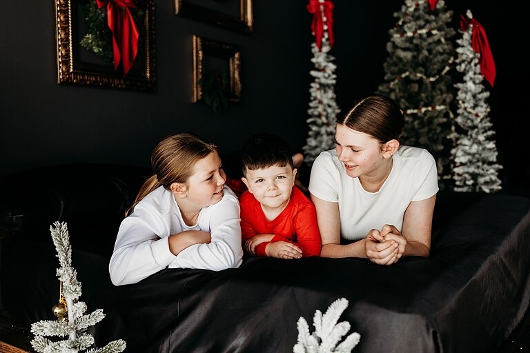 Moody Christmas mini session setup with black bed, snowy Christmas trees, cranberry and popcorn garland, and gold and red holiday accents in a Lake St Louis studio