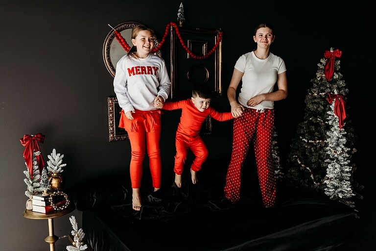 Moody Christmas mini session setup with black bed, snowy Christmas trees, cranberry and popcorn garland, and gold and red holiday accents in a Lake St Louis studio