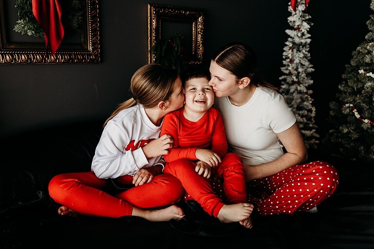 Moody Christmas mini session setup with black bed, snowy Christmas trees, cranberry and popcorn garland, and gold and red holiday accents in a Lake St Louis studio