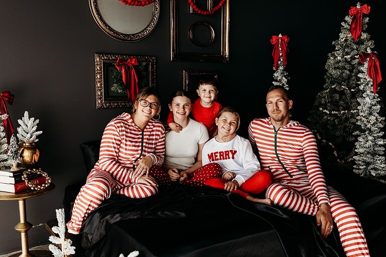 Moody Christmas mini session setup with black bed, snowy Christmas trees, cranberry and popcorn garland, and gold and red holiday accents in a Lake St Louis studio