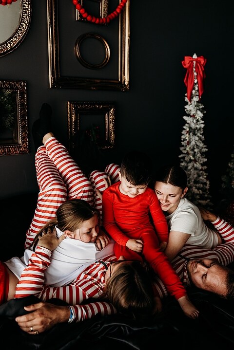 Moody Christmas mini session setup with black bed, snowy Christmas trees, cranberry and popcorn garland, and gold and red holiday accents in a Lake St Louis studio