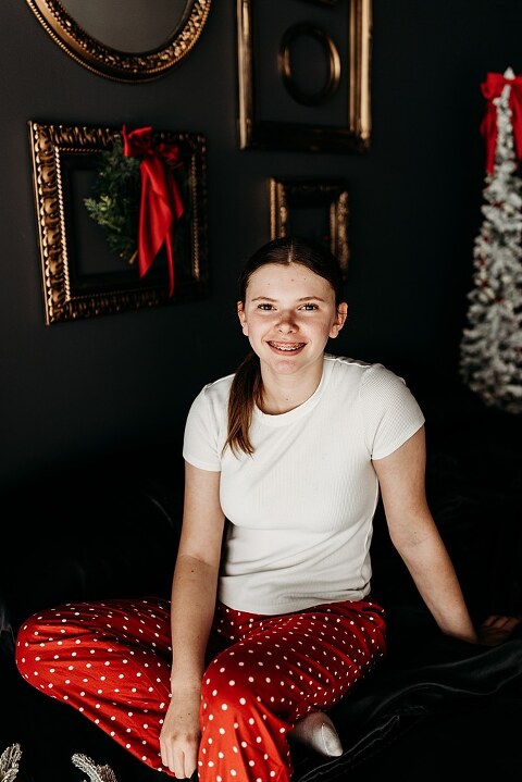 Moody Christmas mini session setup with black bed, snowy Christmas trees, cranberry and popcorn garland, and gold and red holiday accents in a Lake St Louis studio