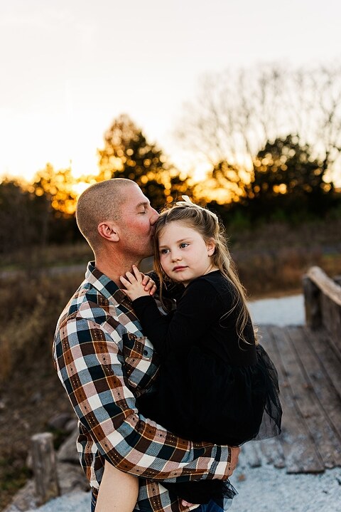 Family standing together at Towne Park in Foristell Missouri during golden hour.
Parents holding their children while laughing in an open field.
Family walking along a tree-lined path at Towne Park.
Kids smiling while standing between their parents during the session.
Close-up of Rob and Taylor hugging with soft light behind them.