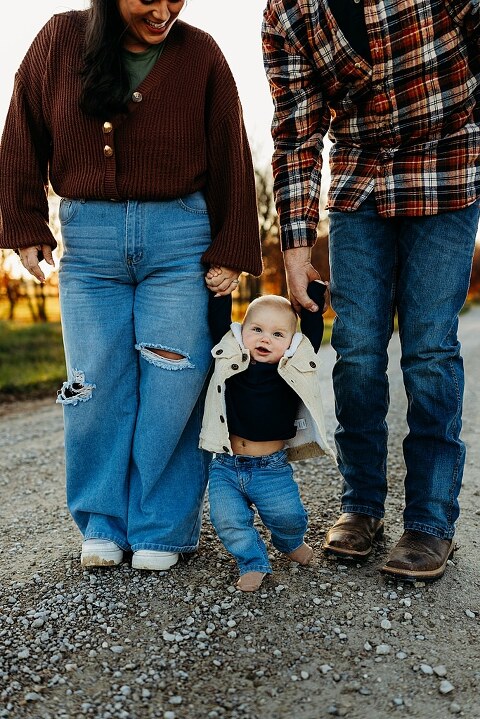 Family holding their baby during a session in High Hill Missouri.
Parents kissing their smiling little boy in warm natural light.
Baby laughing while sitting with his parents on a country path.
Family walking together through a grassy field.
Close-up of baby boy smiling during his milestone session.