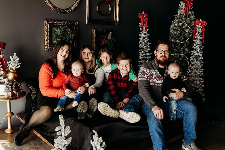 Family sitting on black bed during Christmas Mini Session with trees and garland
Parents holding newborn twins in studio with red and gold holiday details
Children sitting together on bed with Christmas trees behind them
Close up of popcorn and cranberry garland in Christmas Mini setup