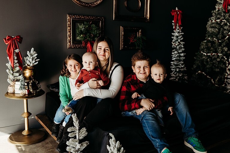 Family sitting on black bed during Christmas Mini Session with trees and garland
Parents holding newborn twins in studio with red and gold holiday details
Children sitting together on bed with Christmas trees behind them
Close up of popcorn and cranberry garland in Christmas Mini setup