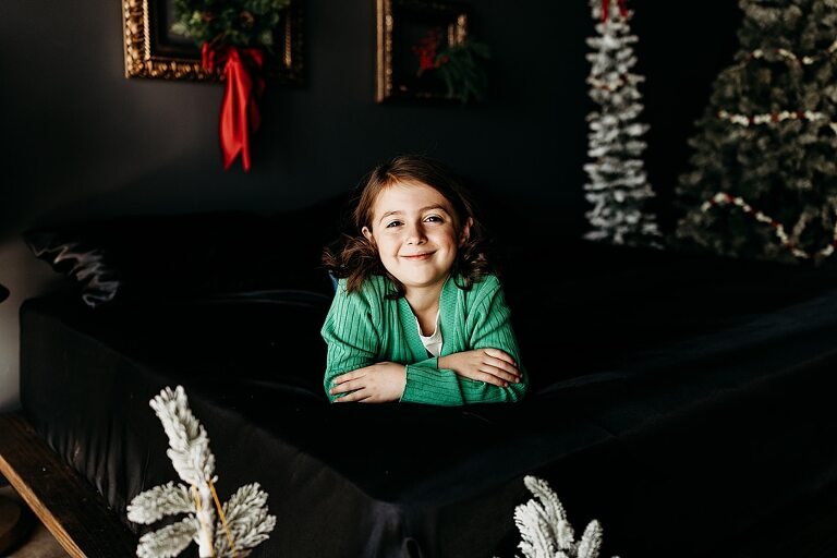 Family sitting on black bed during Christmas Mini Session with trees and garland
Parents holding newborn twins in studio with red and gold holiday details
Children sitting together on bed with Christmas trees behind them
Close up of popcorn and cranberry garland in Christmas Mini setup