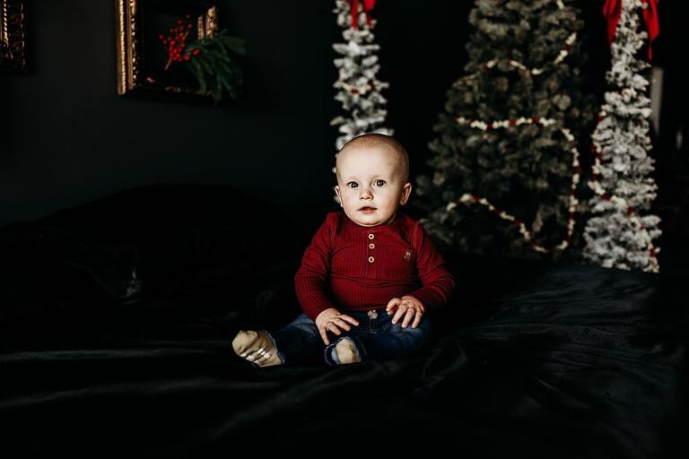 Family sitting on black bed during Christmas Mini Session with trees and garland
Parents holding newborn twins in studio with red and gold holiday details
Children sitting together on bed with Christmas trees behind them
Close up of popcorn and cranberry garland in Christmas Mini setup
