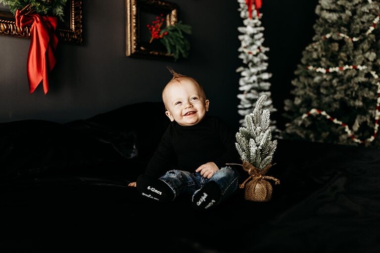 Family sitting on black bed during Christmas Mini Session with trees and garland
Parents holding newborn twins in studio with red and gold holiday details
Children sitting together on bed with Christmas trees behind them
Close up of popcorn and cranberry garland in Christmas Mini setup