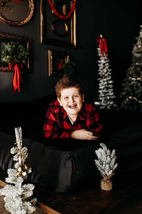 Family sitting on black bed during Christmas Mini Session with trees and garland
Parents holding newborn twins in studio with red and gold holiday details
Children sitting together on bed with Christmas trees behind them
Close up of popcorn and cranberry garland in Christmas Mini setup