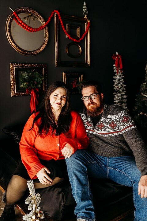 Family sitting on black bed during Christmas Mini Session with trees and garland
Parents holding newborn twins in studio with red and gold holiday details
Children sitting together on bed with Christmas trees behind them
Close up of popcorn and cranberry garland in Christmas Mini setup